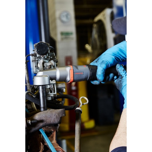 Photo of PROTO J150WA pneumatic ratchet wrench in use by a person wearing blue gloves, shown tightening a bolt in a workshop.