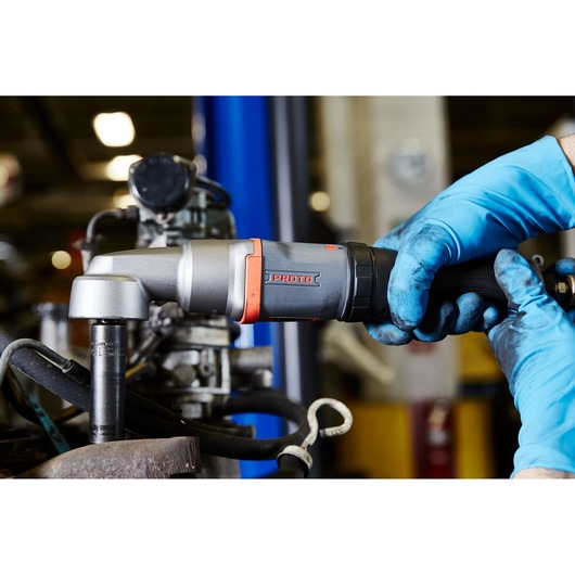 PROTO J150WA pneumatic ratchet wrench in use, held by gloved hands on machinery, close-up view.