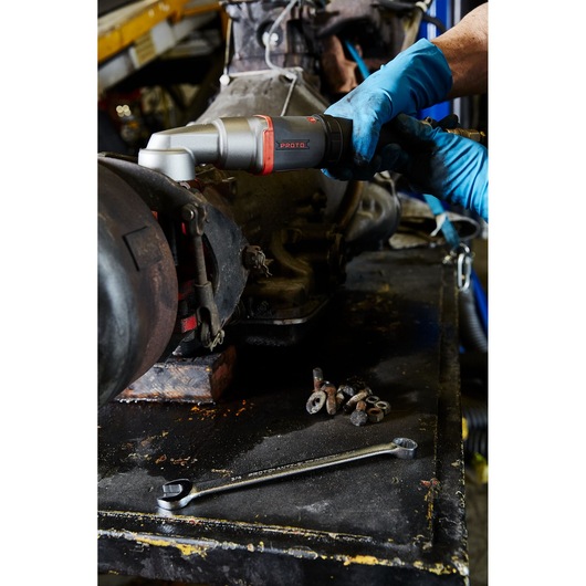 Photo of a PROTO J150WA pneumatic ratchet being used by a gloved hand on machinery, with wrench and bolts on a workbench.