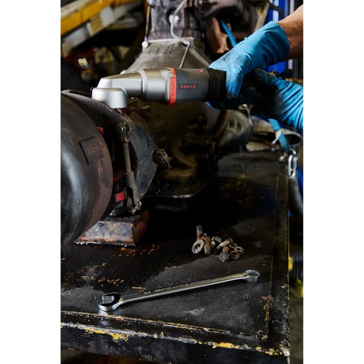 PROTO J150WA pneumatic angle wrench in use by gloved hand on machinery, with a box end wrench and bolts on workbench.