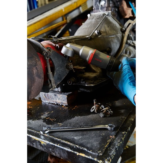 PROTO J150WA cordless ratchet being used on auto part by person with blue gloves, metal parts and wrench on workbench.