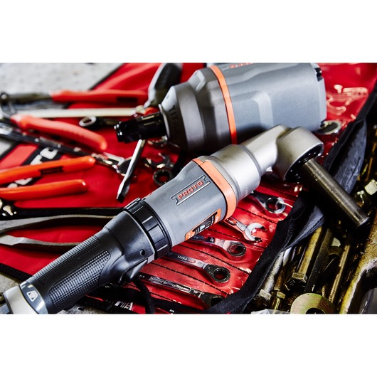 Close-up of a PROTO J150WA power tool, shown resting on a red tool roll with various wrenches and hand tools. The tool is gray with orange accents and has a textured handle.