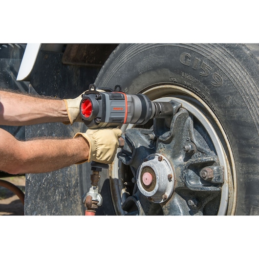 PROTO J199WP pneumatic impact wrench used on large truck wheel, worker wearing gloves.