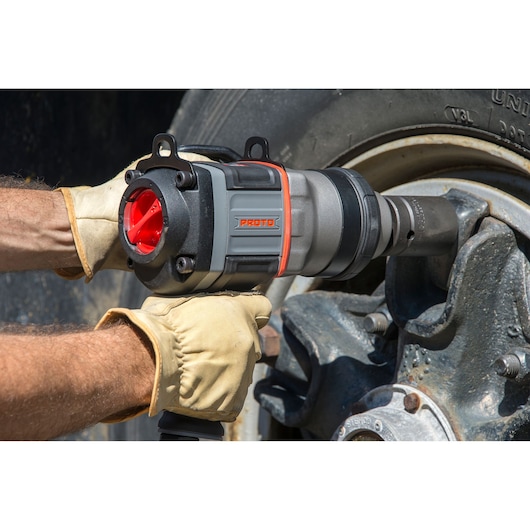 PROTO J199WP impact wrench used by a gloved worker tightening a large wheel lug nut outdoors.