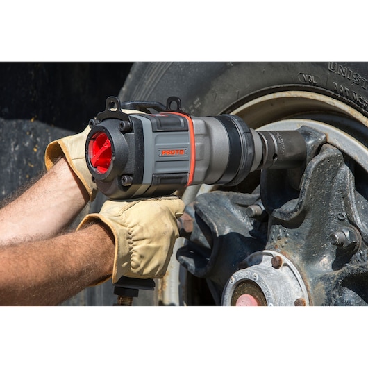 Photo of PROTO J199WP impact wrench in use on a truck wheel, showing gray and red tool held by gloved hands.