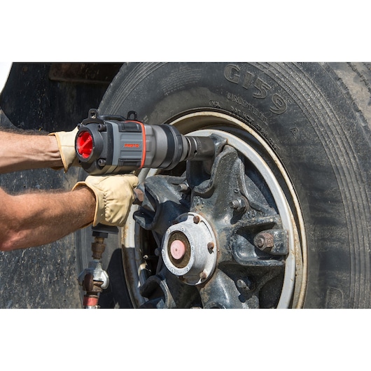 Photo of PROTO J199WP pneumatic impact wrench being used to loosen lug nuts on a large vehicle wheel.