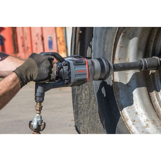 Photo of PROTO J199WP impact wrench being used to tighten lug nuts on a large truck wheel outdoors.