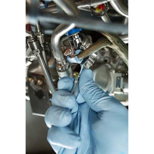 PROTO J4771TA wrench used by gloved hand on metal fittings in industrial machinery, close-up photography.