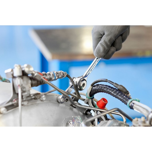 Photo of a gloved hand using a PROTO J5100 ratcheting wrench on machinery with visible wires and metal components.