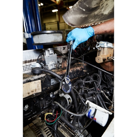 PROTO J5450 ratchet wrench in use on an engine by a gloved hand, automotive garage setting.