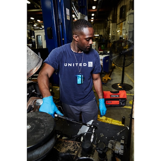 PROTO J5450 red tool bag on the shop floor in the background, black base, visible logo, industrial setting.
