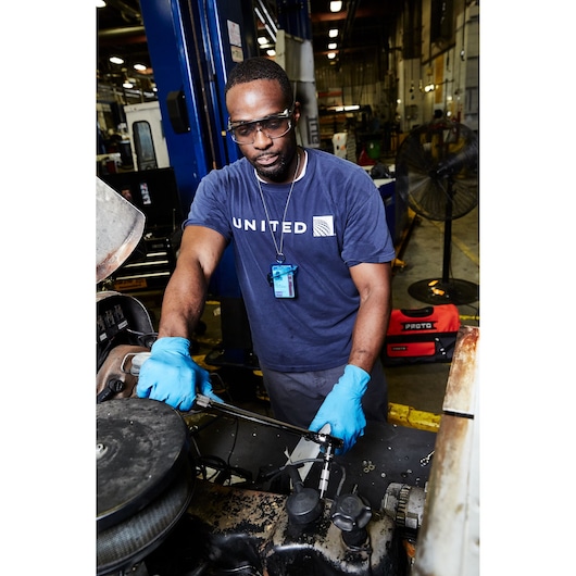 PROTO J5450 red tool bag on the floor behind mechanic working with torque wrench in workshop.