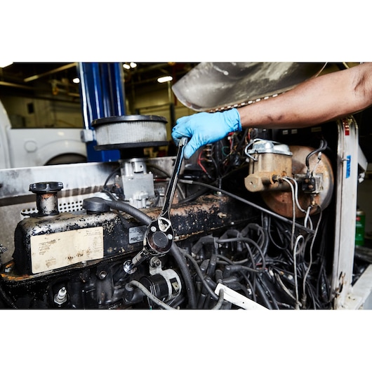 PROTO ratchet wrench J5450 used on engine in workshop, technician with blue gloves working.