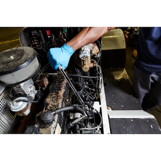 PROTO ratchet J5450 used by a person wearing blue gloves to work on an engine, close-up view.