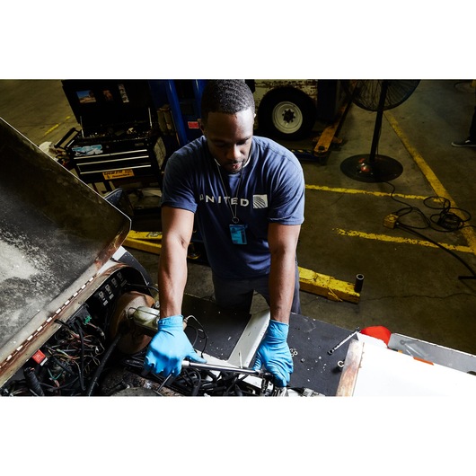 PROTO J5450 hand tool used by mechanic with blue gloves working on engine in industrial workshop, overhead angle.